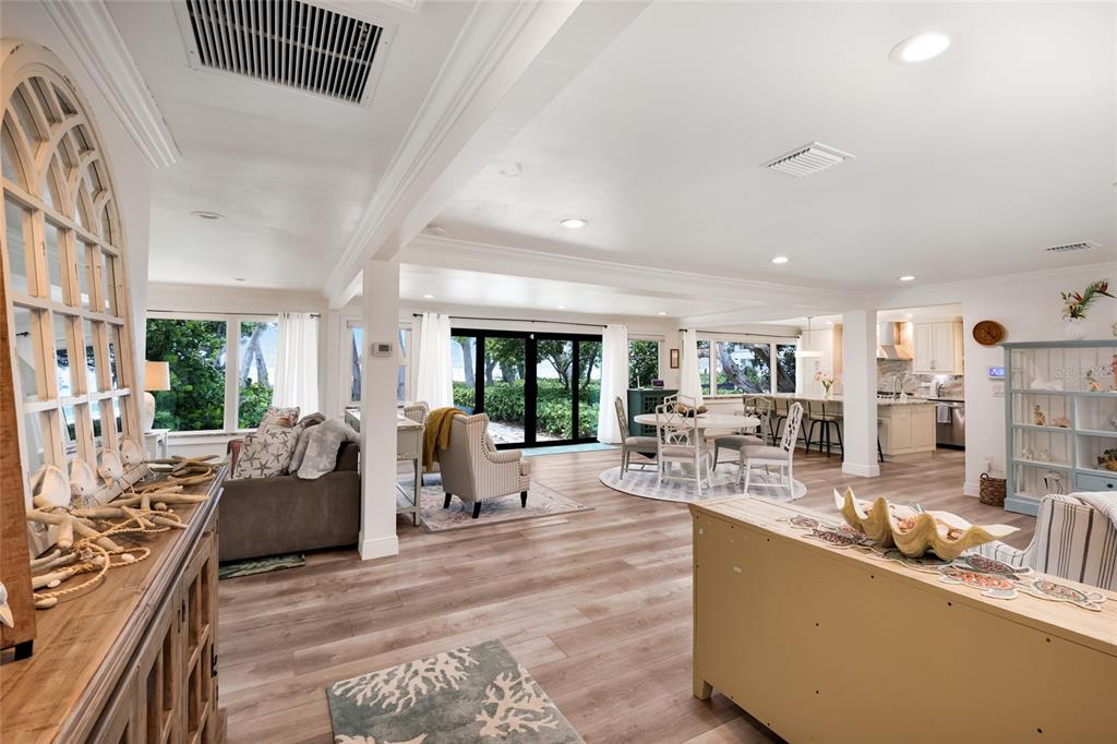 An open-concept living and dining area features light wood flooring, neutral furniture, and large windows — 103 51ST STREET, HOLMES BEACH, FL