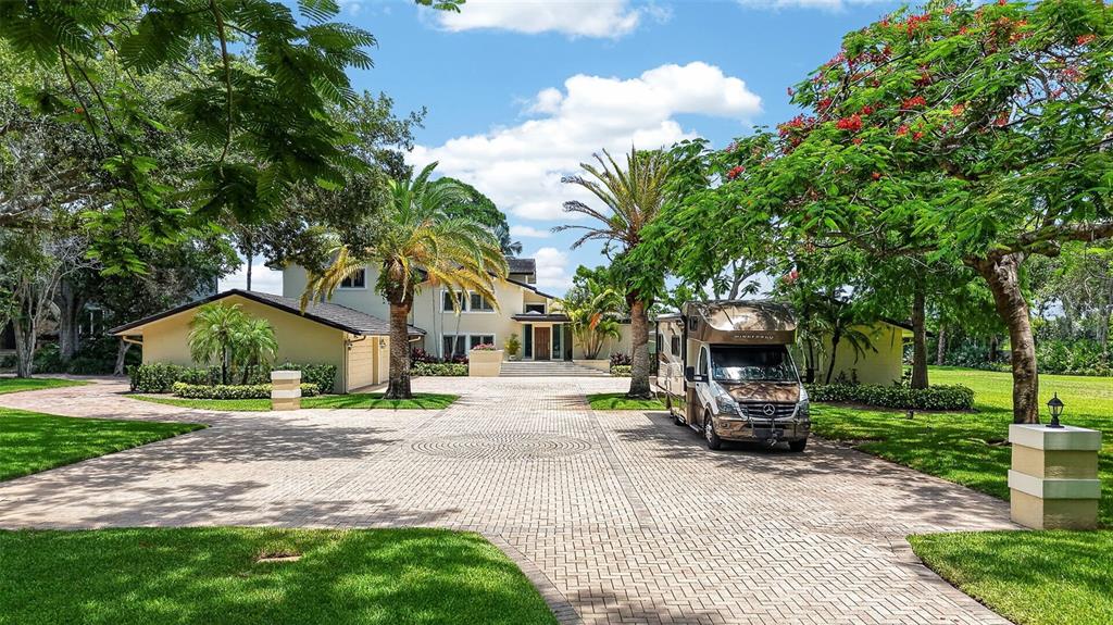 A large house with a paved driveway and a parked motorhome sits among lush trees — 6305 BURNING TREE DRIVE, SEMINOLE, FL