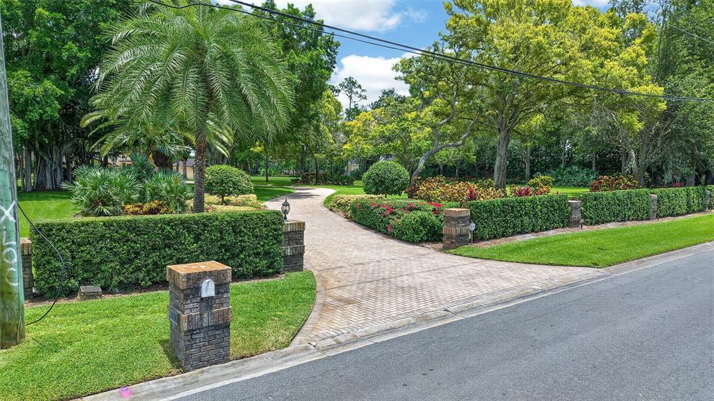A paved driveway leads through a landscaped yard with manicured hedges and mature trees — 6305 BURNING TREE DRIVE, SEMINOLE, FL