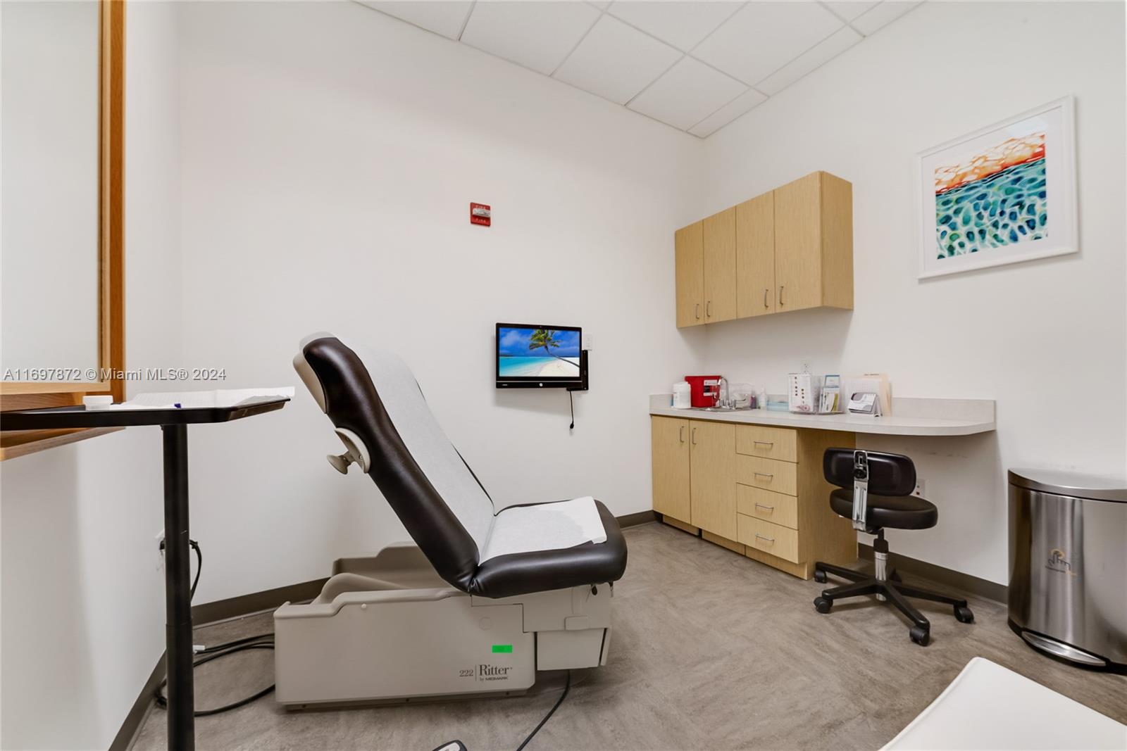 A medical examination room features a treatment chair, cabinetry, a desk, and a wall-mounted monitor — 6705 Red Rd # 518, Coral Gables FL 33143, CORAL GABLES, FL