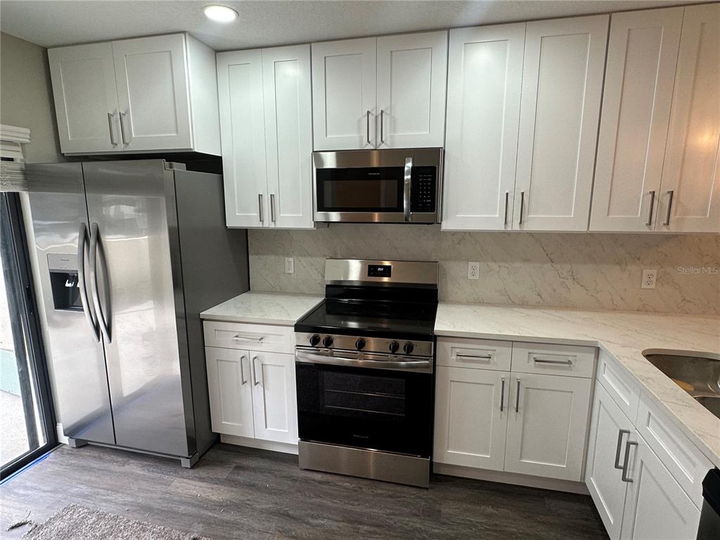 A modern kitchen features white cabinets, stainless steel appliances, and a marble-patterned backsplash — 717 OAK PARK PLACE, BRANDON, FL