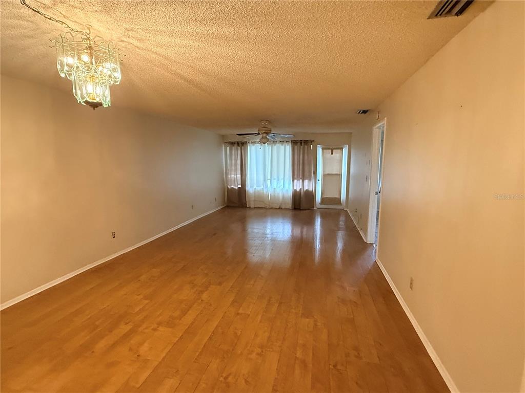 An empty living room features hardwood floors, a ceiling fan, and a decorative chandelier — 3832 TEESIDE DRIVE UNIT 4, NEW PORT RICHEY, FL