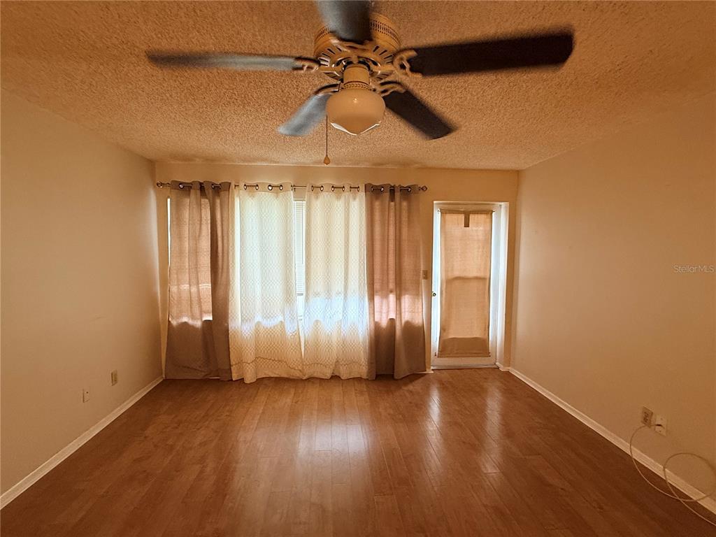 An empty room with wood-look flooring, a ceiling fan, and curtains covering a window and door — 3832 TEESIDE DRIVE UNIT 4, NEW PORT RICHEY, FL