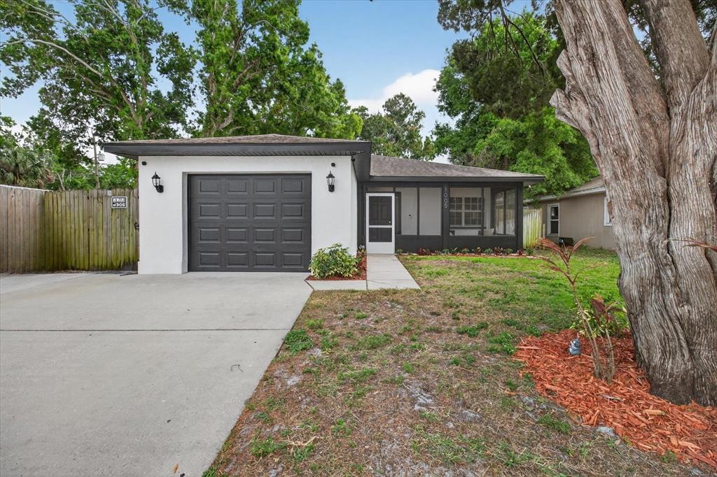 A single-story house with a white stucco exterior, a dark garage door, and a screened porch — 1005 13TH AVENUE NW, LARGO, FL