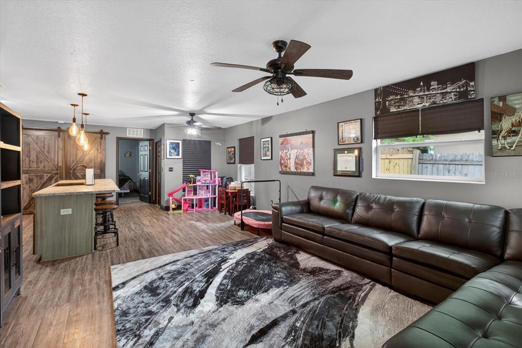 A living room with a large leather sectional, wood-look flooring, and an open kitchen area — 1005 13TH AVENUE NW, LARGO, FL