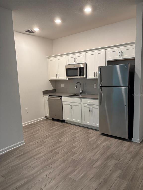 A kitchen features white cabinets, stainless steel appliances, gray countertops, and wood-look tile flooring — 6267 LAKEPINE STREET, ST CLOUD, FL