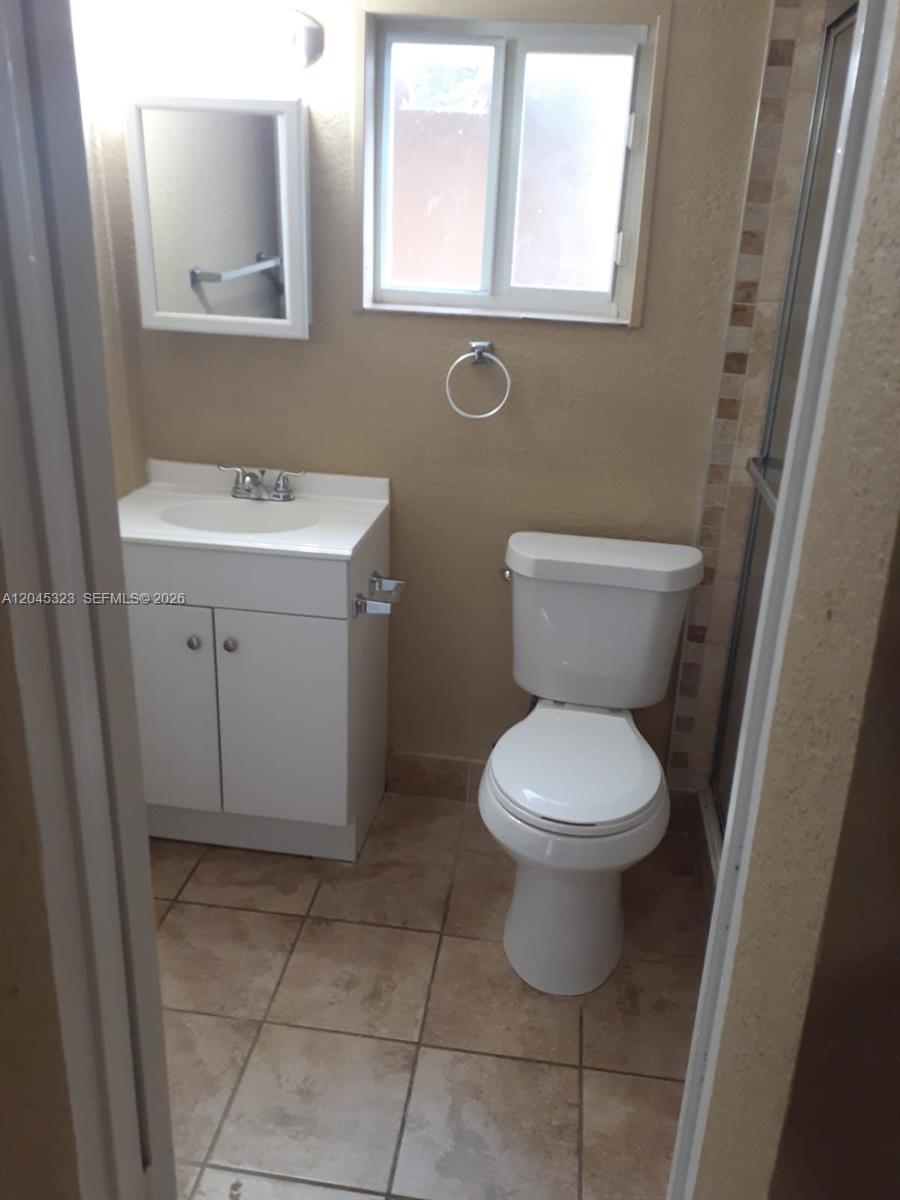 A small bathroom features a white vanity, a toilet, and a window above the sink — MIAMI, FL
