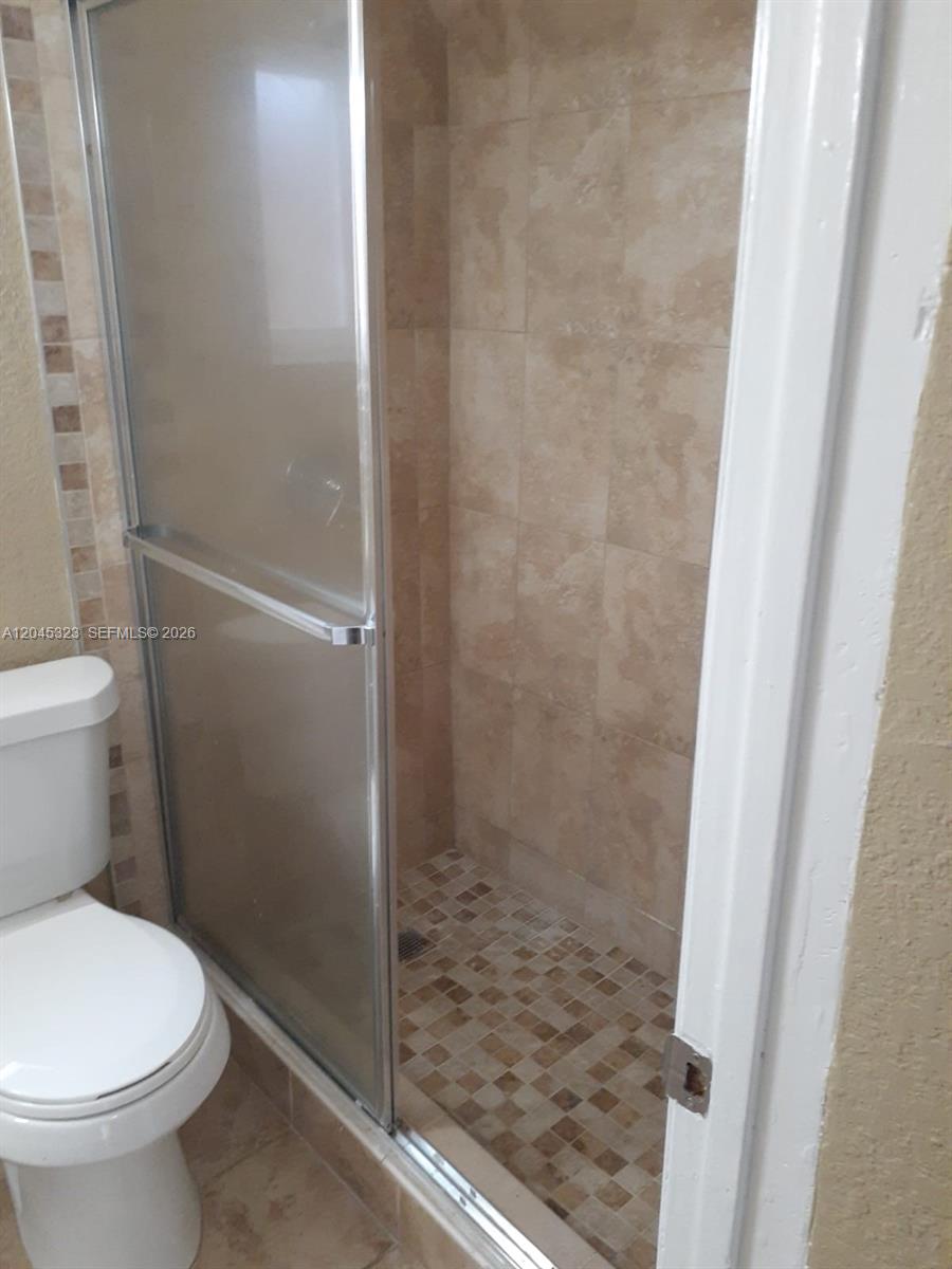 A bathroom features a tiled walk-in shower with a glass door next to a toilet — MIAMI, FL