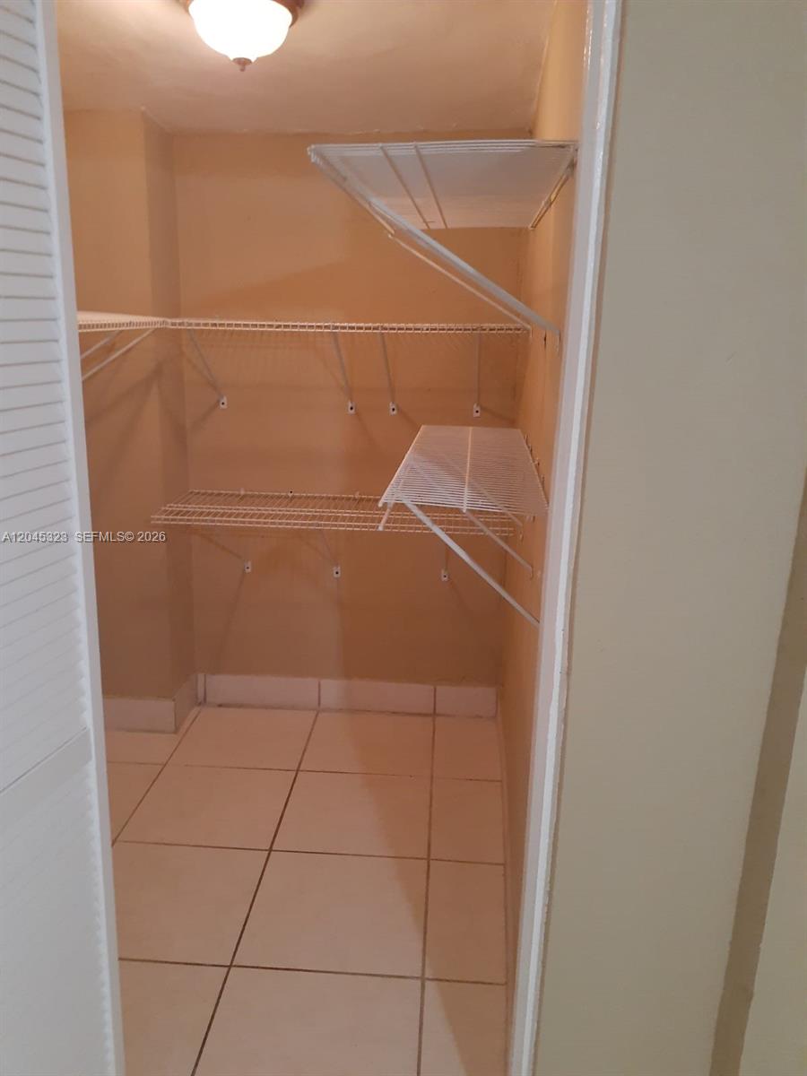 A small walk-in closet features white wire shelving and light-colored floor tiles — MIAMI, FL