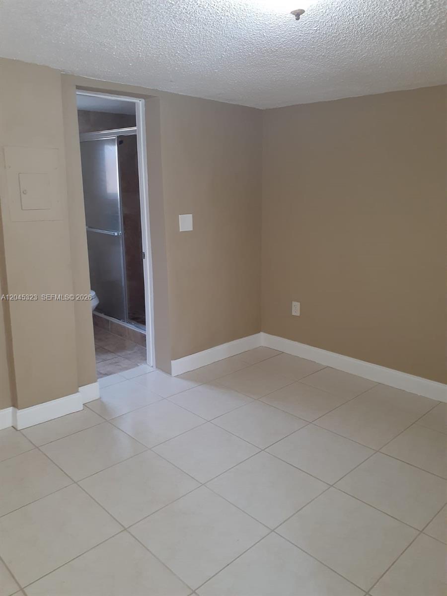 An empty room with beige walls, white baseboards, and light-colored floor tiles — MIAMI, FL