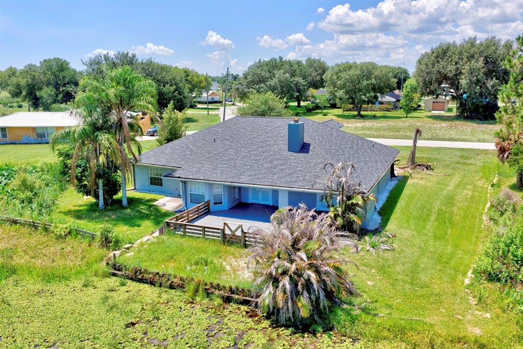 An aerial view shows a single-story house with a dark roof, deck, and backyard pond — 110 GATES AVENUE, LAKE PLACID, FL