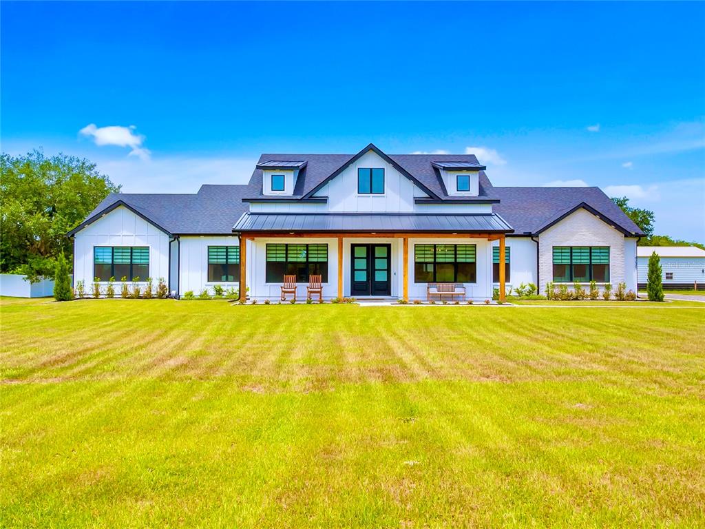 A white farmhouse with a dark metal roof, dormer windows, and a covered front porch — 4230 TUCKER AVENUE, ST CLOUD, FL