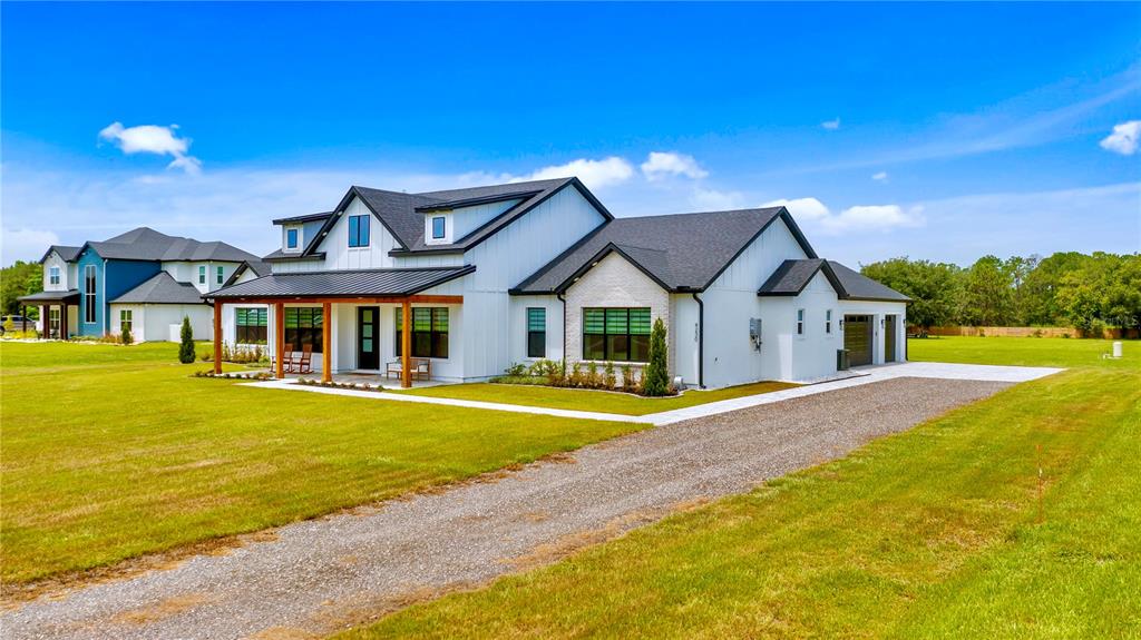 A modern white farmhouse with a metal roof and a gravel driveway sits on grass — 4230 TUCKER AVENUE, ST CLOUD, FL