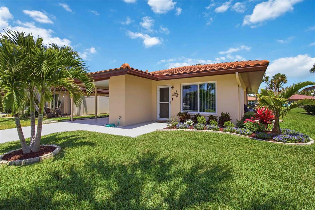 A single-story house with a tile roof, carport, and landscaped front yard under a blue sky — 3303 CAMBRIDGE AVENUE, BRADENTON, FL