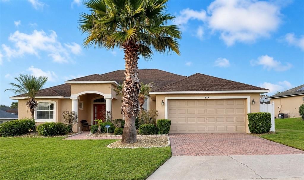 A single-story house with a tan stucco exterior, a brick driveway, and a palm tree — 615 DOLCETTO DRIVE, DAVENPORT, FL