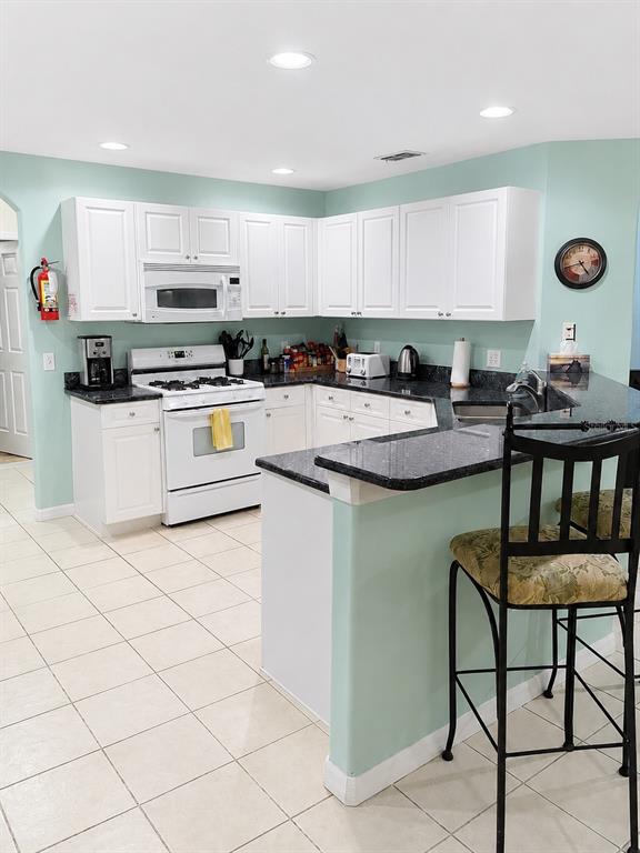 A kitchen features white cabinets, dark countertops, a white stove, and light green walls — 615 DOLCETTO DRIVE, DAVENPORT, FL