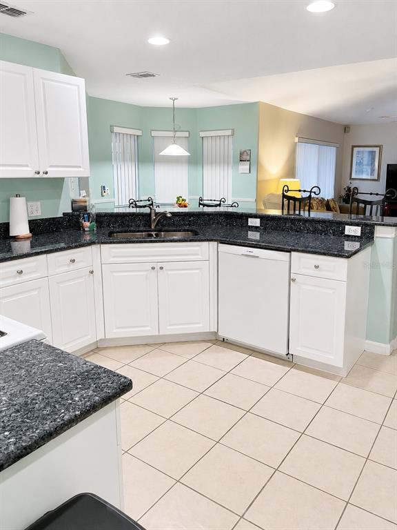 A kitchen features white cabinets, dark granite countertops, and light-colored tile flooring — 615 DOLCETTO DRIVE, DAVENPORT, FL