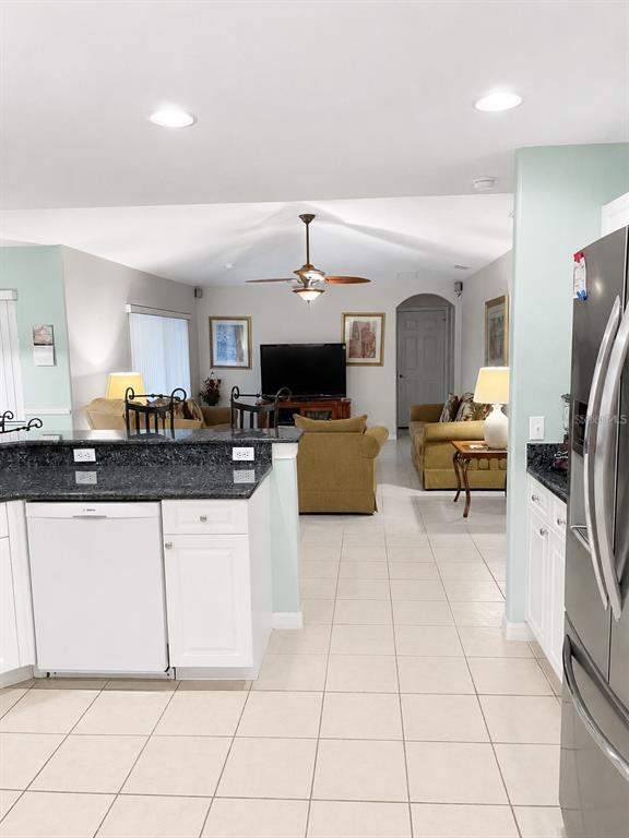 A kitchen with dark granite countertops overlooks a living room with a ceiling fan — 615 DOLCETTO DRIVE, DAVENPORT, FL