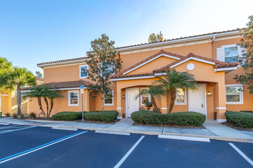 A two-story tan stucco townhouse features a tiled roof, palm trees, and parking spaces — 2683 CORVETTE LANE, KISSIMMEE, FL