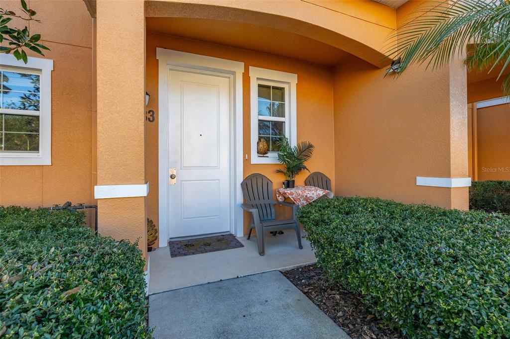 The exterior of a home features an orange stucco wall, a white door, and chairs — 2683 CORVETTE LANE, KISSIMMEE, FL