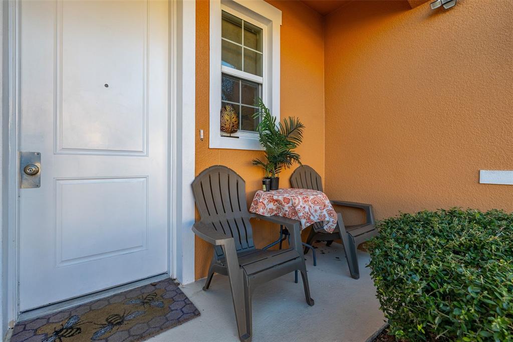 A front porch features two plastic chairs, a small table, and a bee-patterned doormat — 2683 CORVETTE LANE, KISSIMMEE, FL