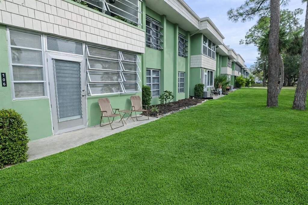 A green two-story apartment building with a patio, lawn, and trees in the foreground — 21280 BRINSON AVENUE UNIT 106, PORT CHARLOTTE, FL