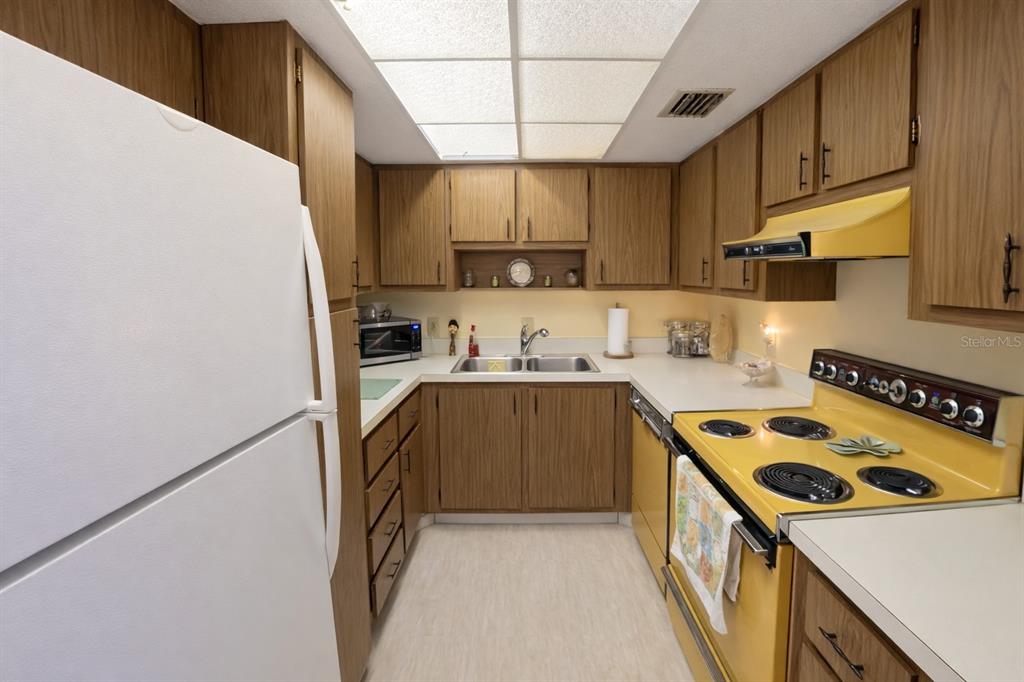 A galley kitchen features wood cabinets, yellow appliances, and a white refrigerator — 21280 BRINSON AVENUE UNIT 106, PORT CHARLOTTE, FL