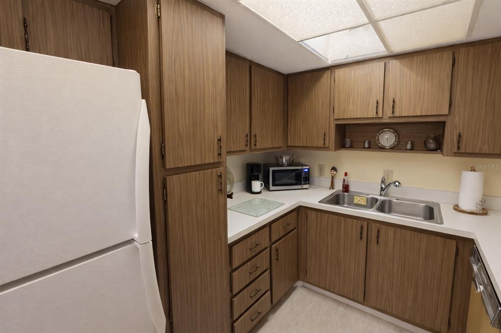 A kitchen features wood-grain cabinets, a white refrigerator, a double sink, and a microwave — 21280 BRINSON AVENUE UNIT 106, PORT CHARLOTTE, FL