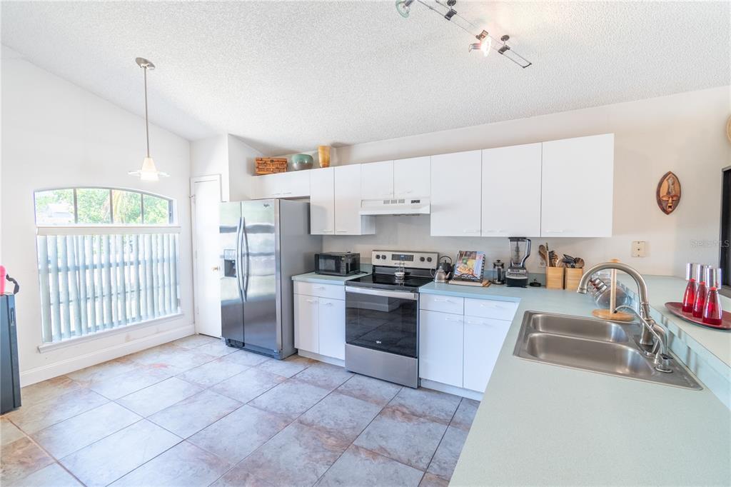 A kitchen features white cabinets, stainless steel appliances, light blue countertops, and tile flooring — 5501 CHATHAM WOODS COURT, ORLANDO, FL