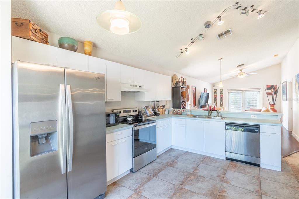 A kitchen with white cabinets, stainless steel appliances, and tile flooring in an open layout — 5501 CHATHAM WOODS COURT, ORLANDO, FL