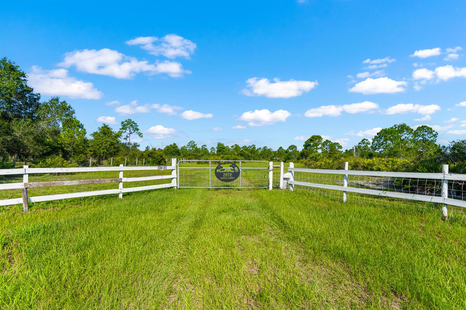 A white wooden fence surrounds a grassy field with a metal gate at the entrance — 2872 Secretariat Drive, FL 33935, FL
