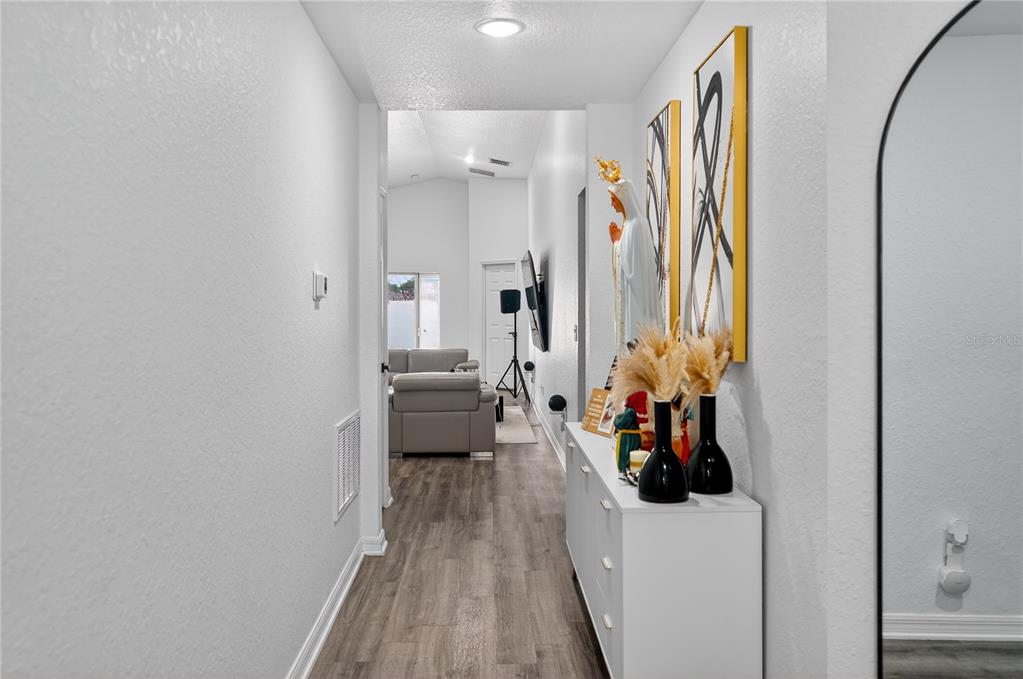 A hallway with wood-look flooring leads to a living area with a gray sofa — 226 POLERMO AVENUE, ST CLOUD, FL