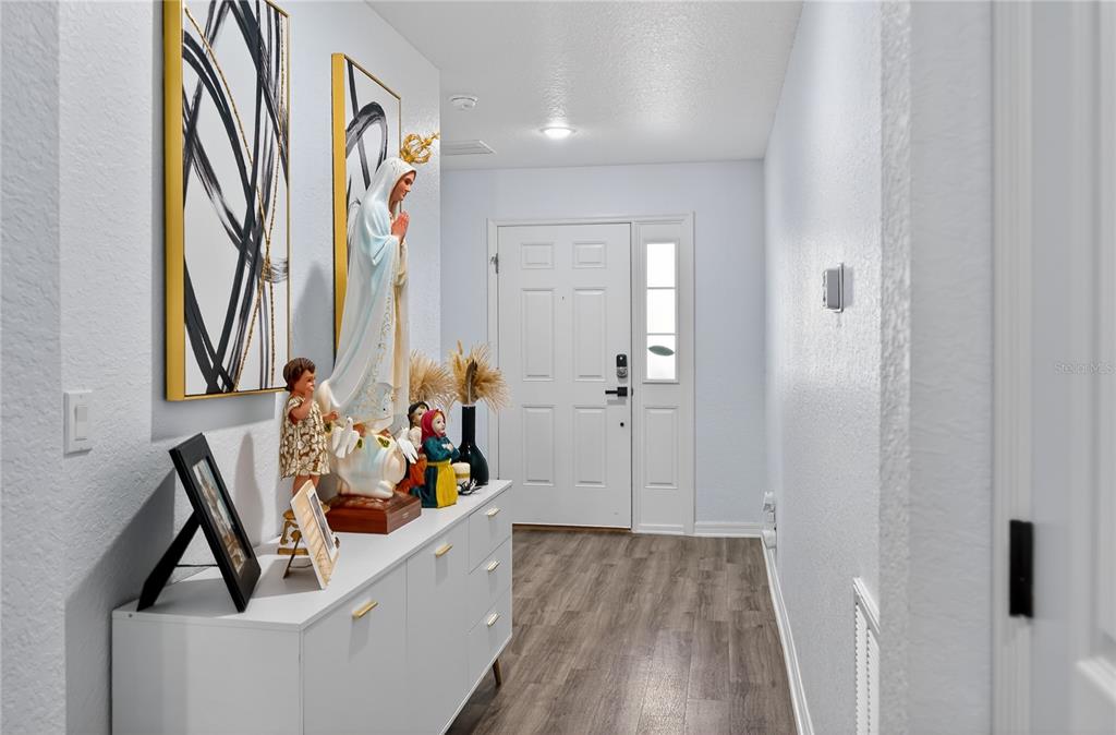 An entryway features a white console table, religious statues, wall art, and wood-look flooring — 226 POLERMO AVENUE, ST CLOUD, FL