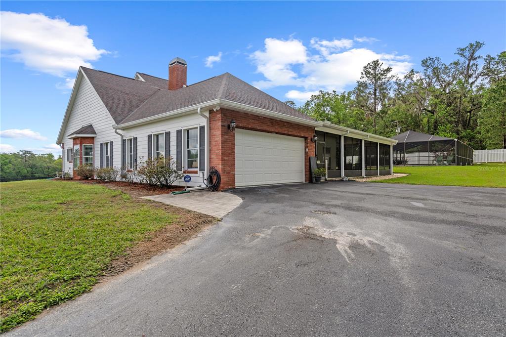 A white house with a brick garage, a screened-in porch, and a paved driveway — 12345 CITRUS WAY, BROOKSVILLE, FL