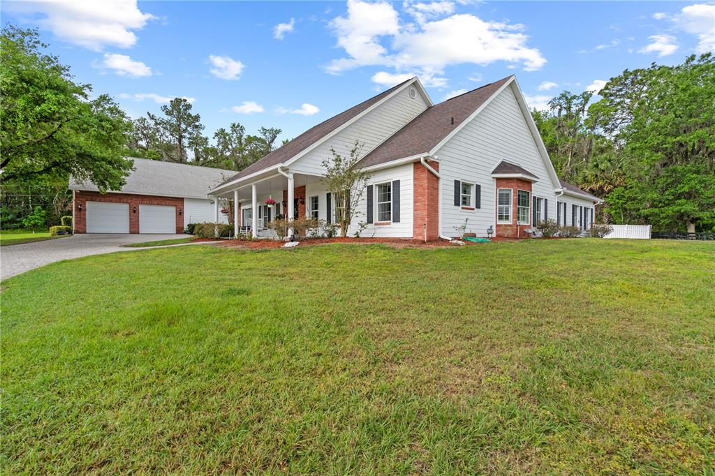 A white house with brick accents, a covered porch, and an attached two-car garage — 12345 CITRUS WAY, BROOKSVILLE, FL