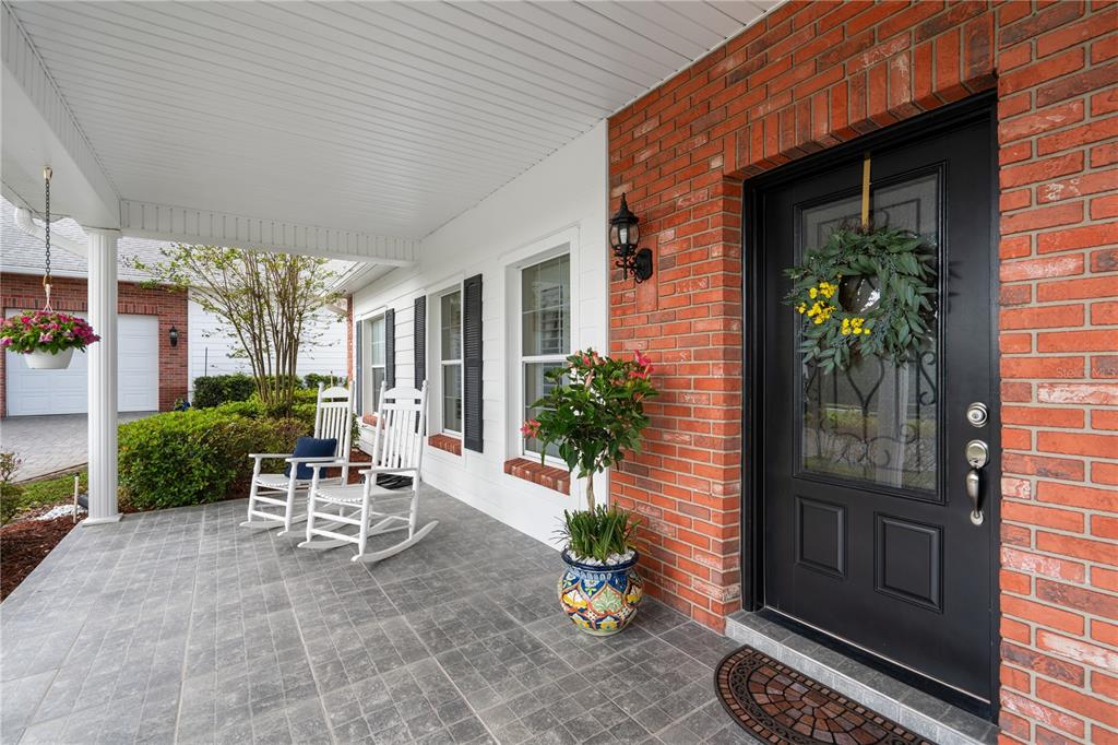 A covered front porch features gray tiled flooring, white rocking chairs, and a black door — 12345 CITRUS WAY, BROOKSVILLE, FL