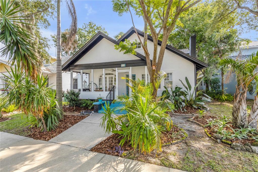 A white bungalow with a dark-trimmed roof and a screened front porch sits behind landscaping — 407 MAGNOLIA STREET, NEW SMYRNA BEACH, FL