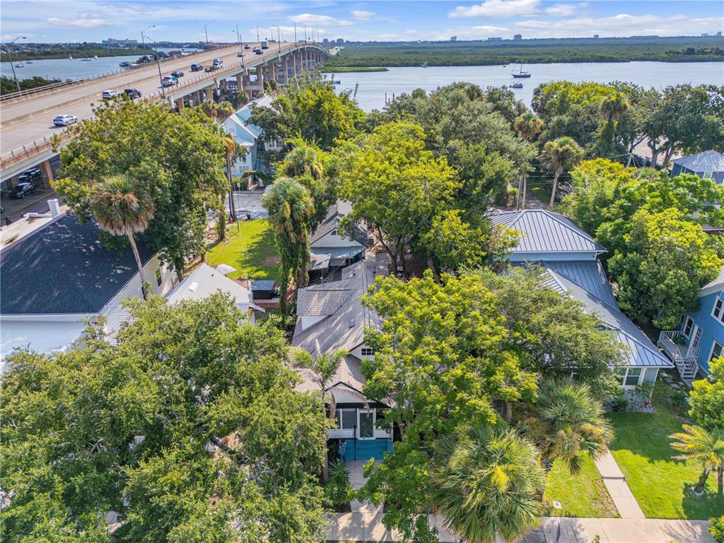 An aerial view shows a house surrounded by trees near a large bridge and water — 407 MAGNOLIA STREET, NEW SMYRNA BEACH, FL