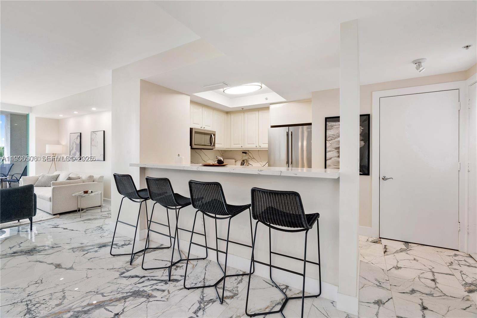 A kitchen with white cabinets and a breakfast bar faces a living area with marble floors — 3400 SW 27th Ave # 605, Miami FL 33133, MIAMI, FL
