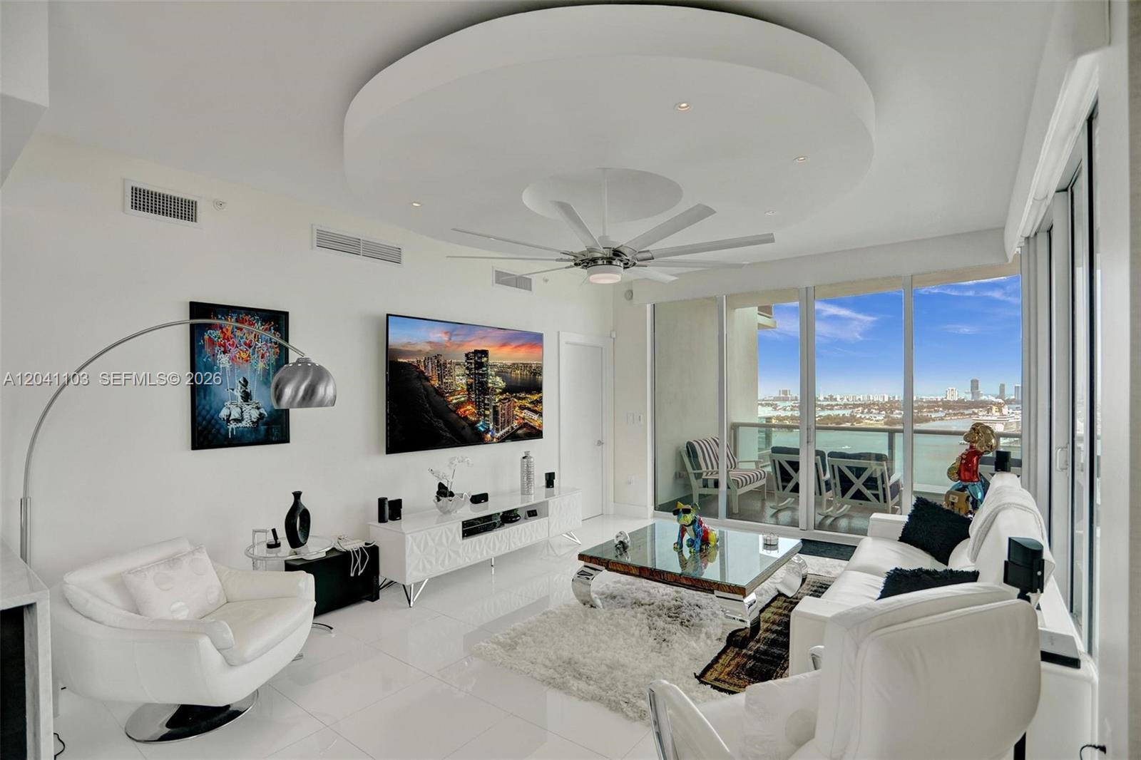 A modern living room features white furniture, a circular ceiling detail, and floor-to-ceiling balcony windows — 900 Biscayne Blvd # 2901, Miami FL 33132, MIAMI, FL