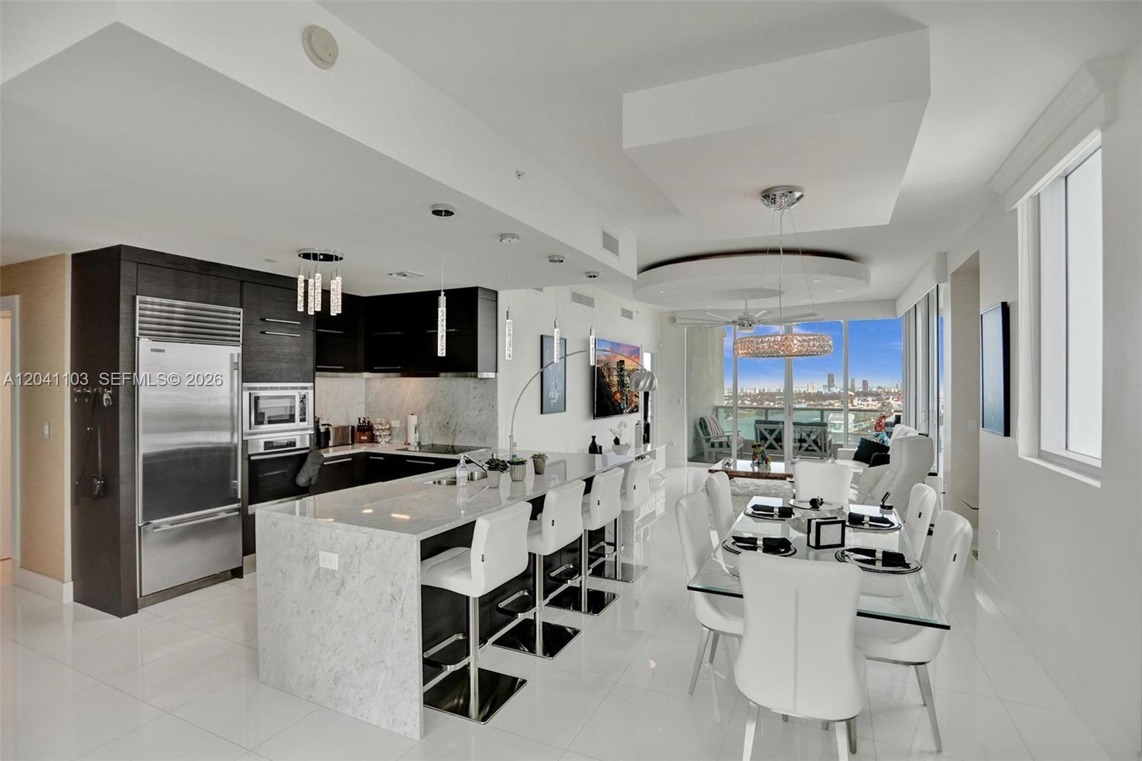 A modern kitchen with marble countertops and white bar stools opens to a dining area — 900 Biscayne Blvd # 2901, Miami FL 33132, MIAMI, FL