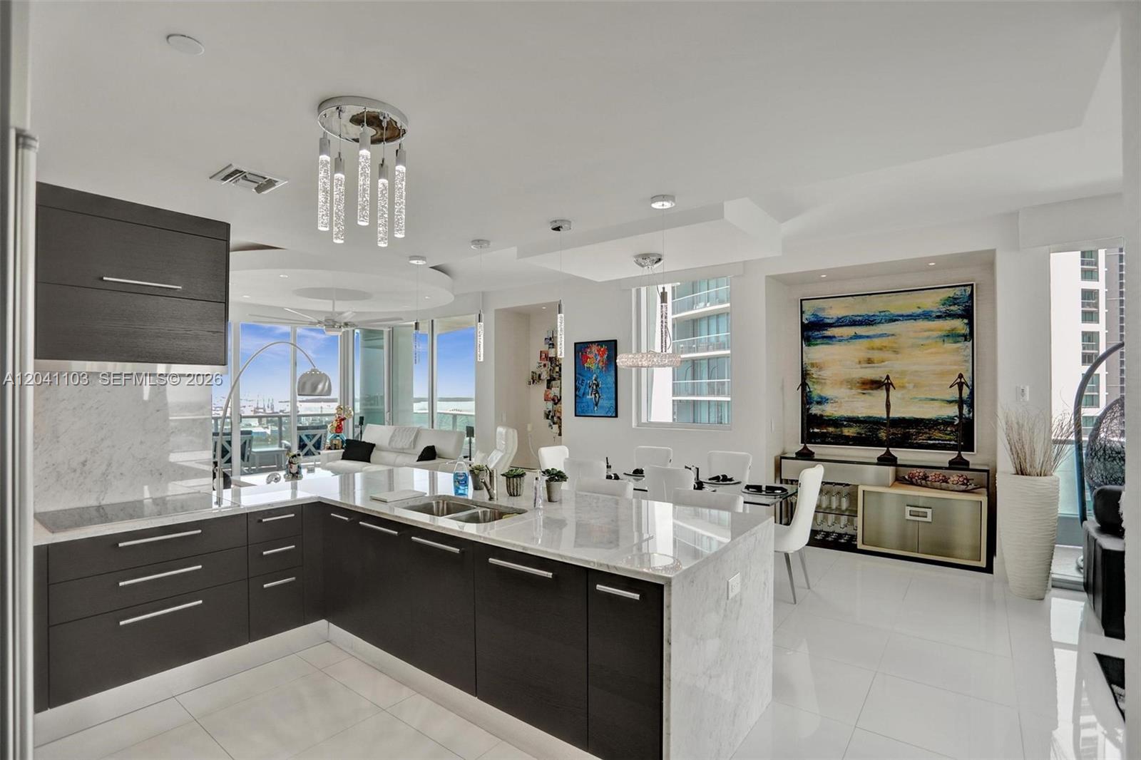 A modern kitchen with dark cabinetry and a marble island overlooks a bright living area — 900 Biscayne Blvd # 2901, Miami FL 33132, MIAMI, FL