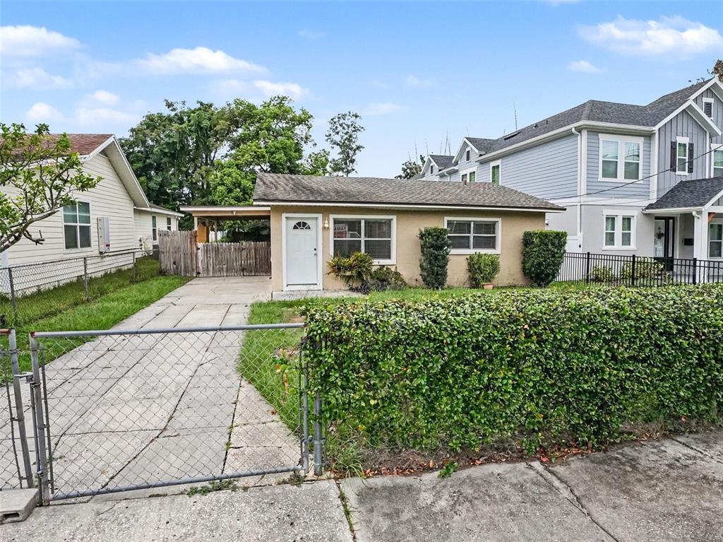 A single-story tan house with a carport and a chain-link fence in the front yard — 1624 HAVEN DRIVE, ORLANDO, FL