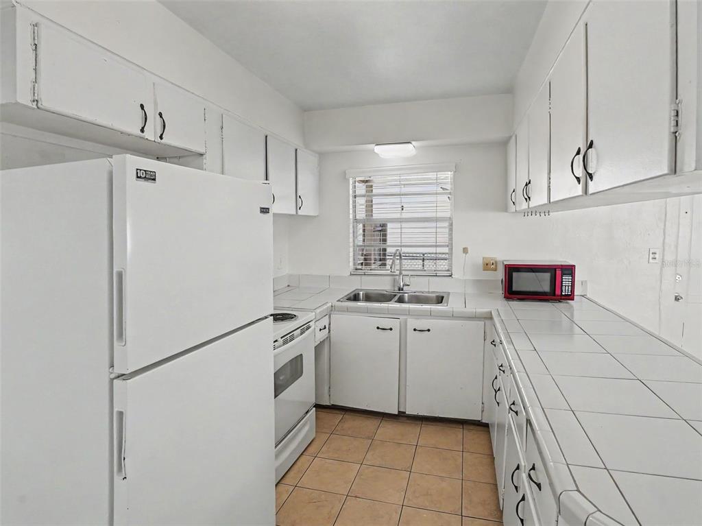 A galley kitchen features white cabinets, white tile countertops, a white refrigerator, and tiled floors — 1624 HAVEN DRIVE, ORLANDO, FL