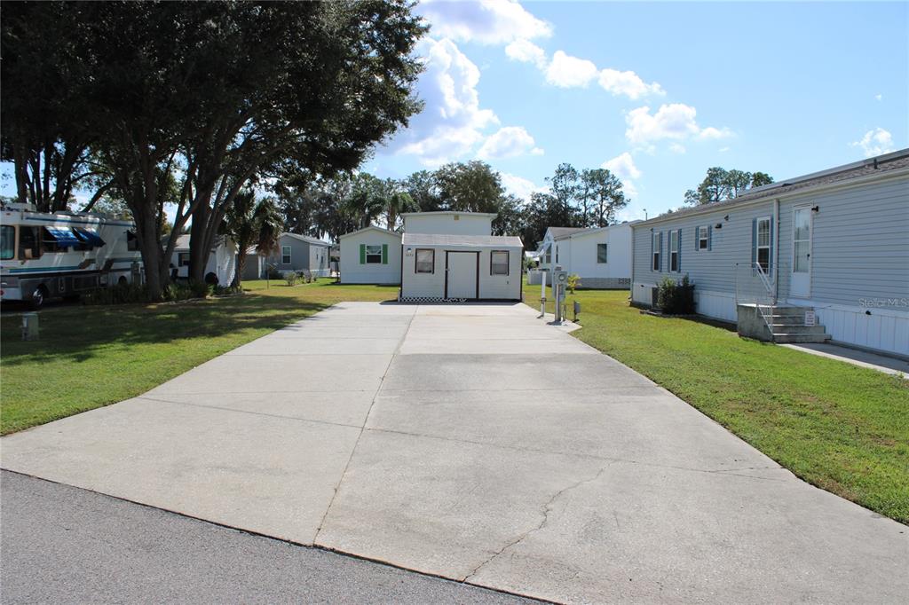 A concrete driveway leads to a small shed between two mobile homes under a blue sky — 5133 SHORE LINE DRIVE, POLK CITY, FL