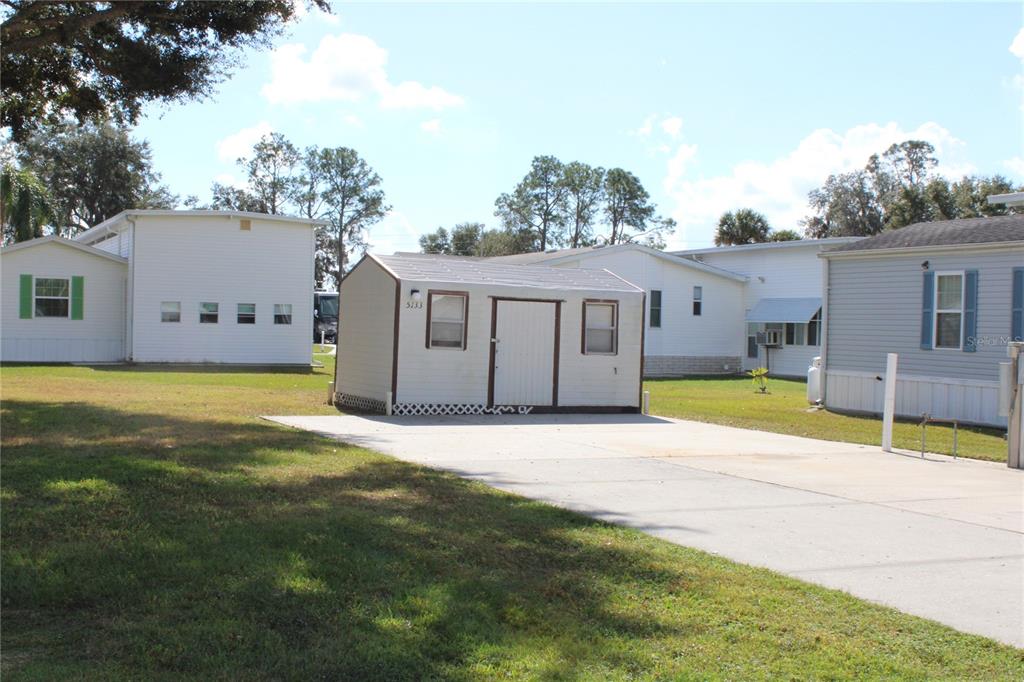 A small, light-colored storage shed sits on a concrete driveway between two mobile homes — 5133 SHORE LINE DRIVE, POLK CITY, FL