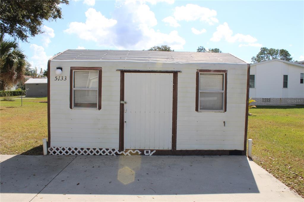A small, white, rectangular storage shed with two windows and a central door sits outdoors — 5133 SHORE LINE DRIVE, POLK CITY, FL