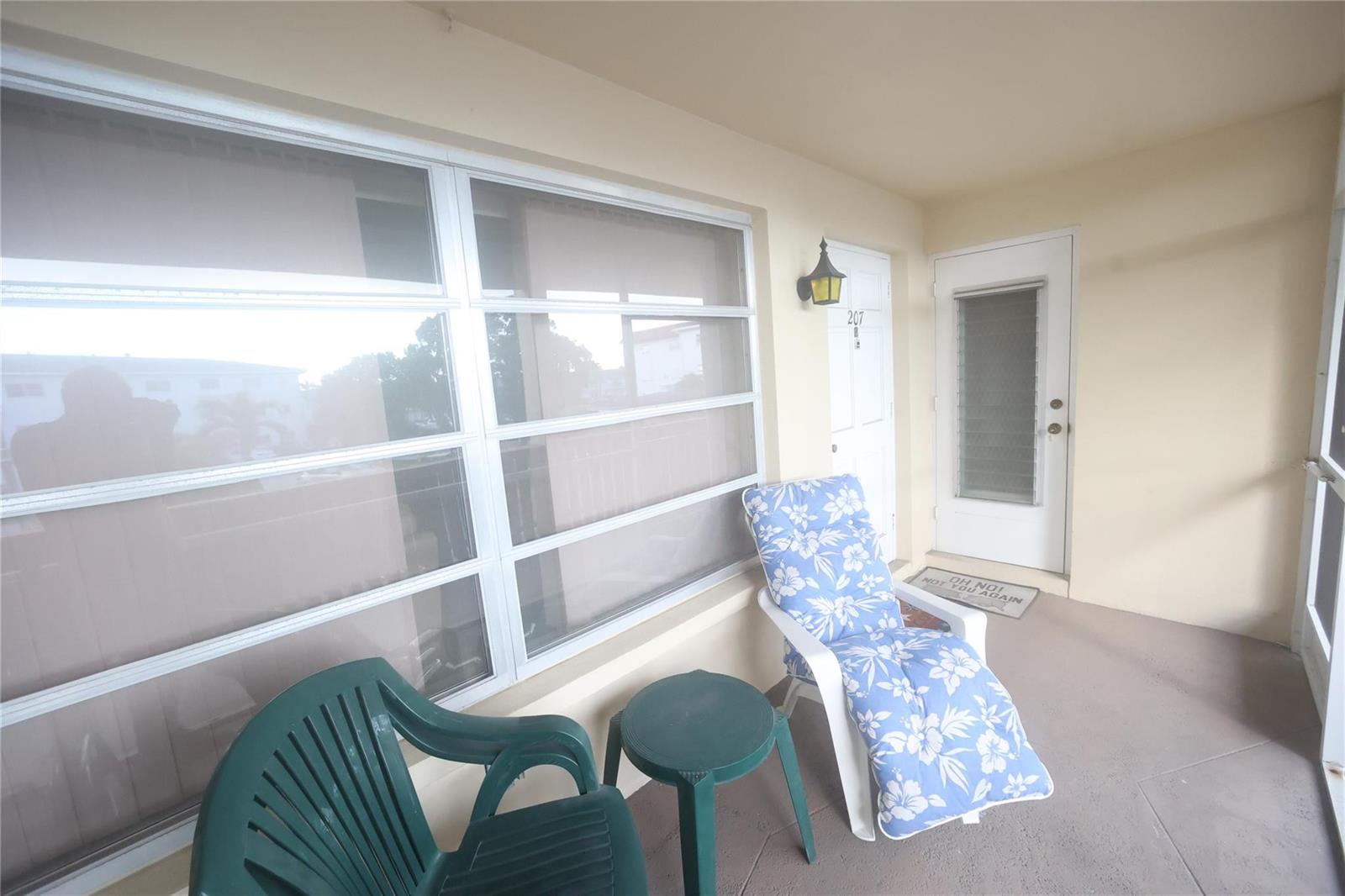 A covered balcony features a large window, two chairs, a small table, and two doors — 601 Pine Drive # 207, Pompano Beach FL 33060, POMPANO BEACH, FL