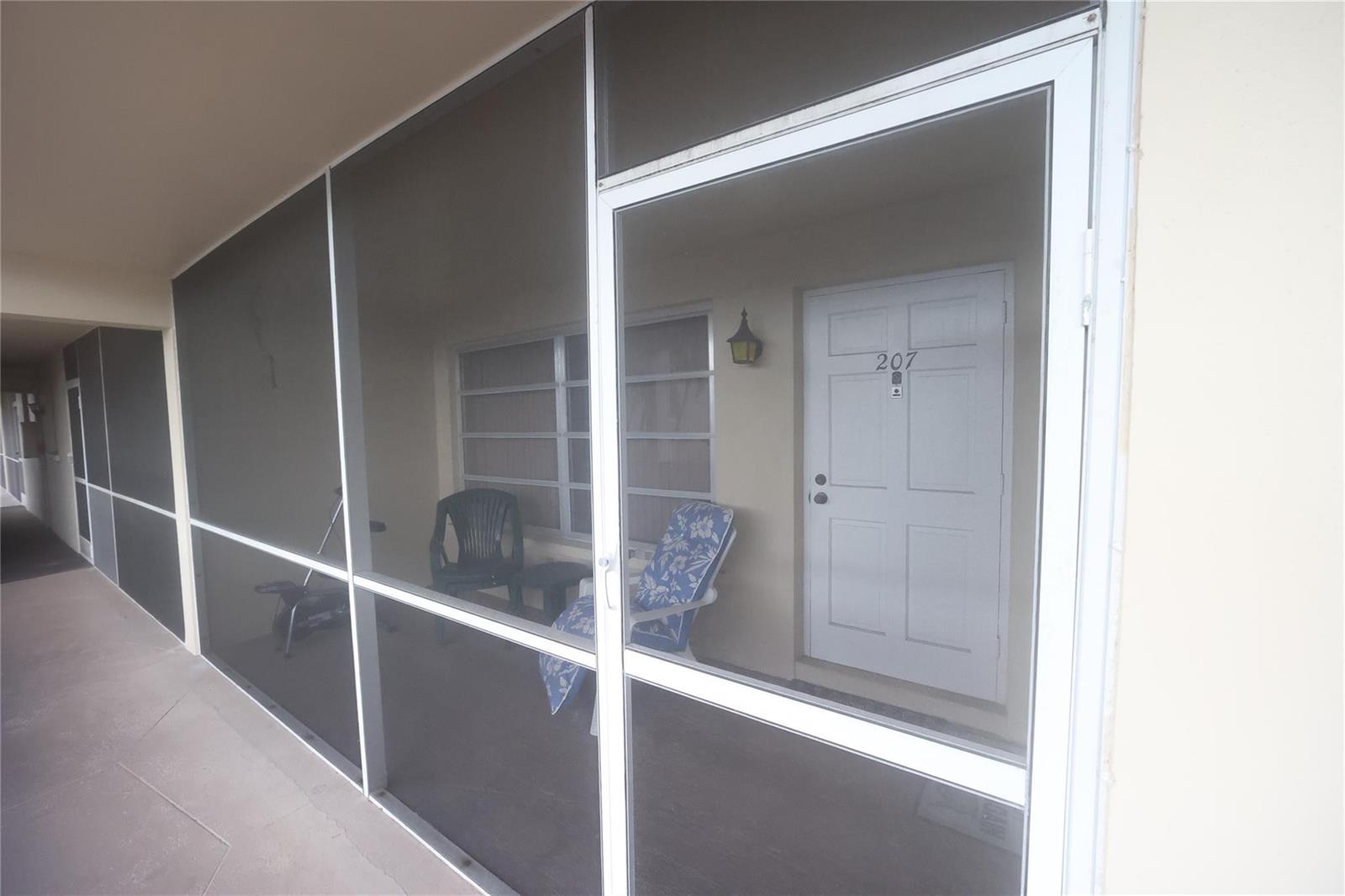 A screened-in porch features a white door labeled 207 and two outdoor chairs — 601 Pine Drive # 207, Pompano Beach FL 33060, POMPANO BEACH, FL