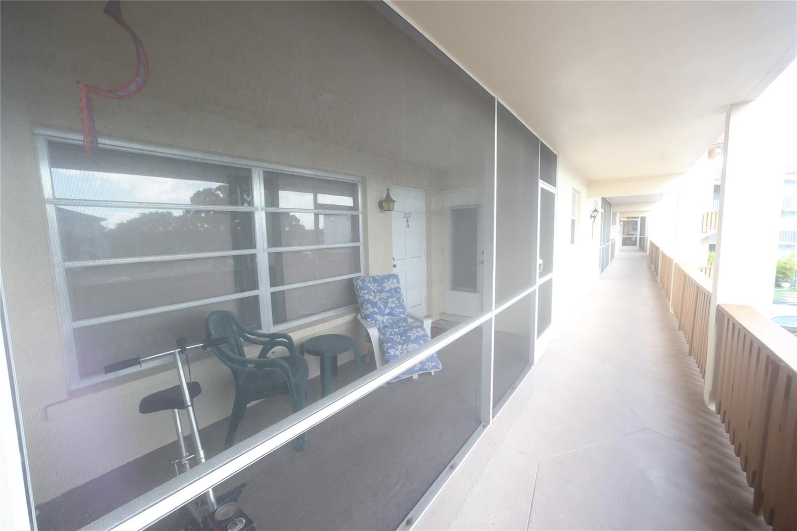 A screened-in balcony with outdoor furniture and a scooter overlooks an exterior apartment hallway — 601 Pine Drive # 207, Pompano Beach FL 33060, POMPANO BEACH, FL